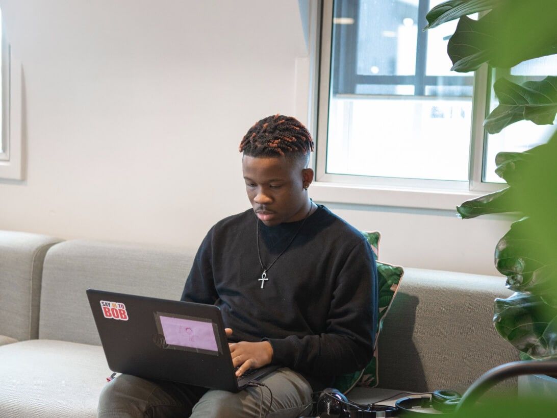 A Multiverse apprentice works on his laptop in a naturally lit office next to some tropical plants.