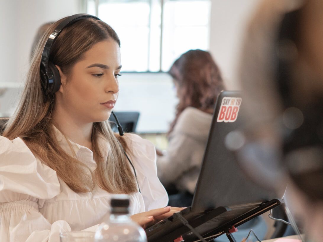 A data fellowship apprentice types on her laptop in a brightly lit open plan office whilst she listens to music through her headphones.